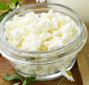 A glass bowl of white cheese on top of a wooden table.