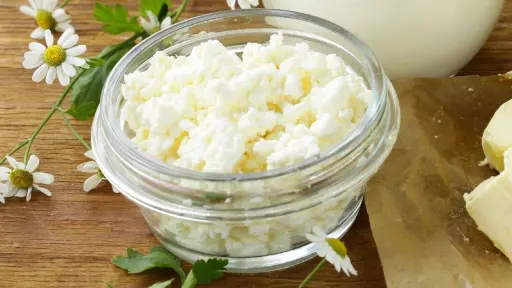 A glass bowl of white cheese on top of a wooden table.