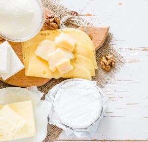 A wooden cutting board topped with cheese next to nuts.