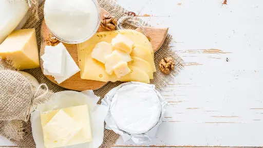 A wooden cutting board topped with cheese next to nuts.