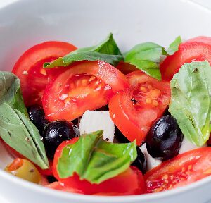 A bowl of salad with tomatoes, olives and spinach.