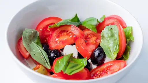 A bowl of salad with tomatoes, olives and spinach.